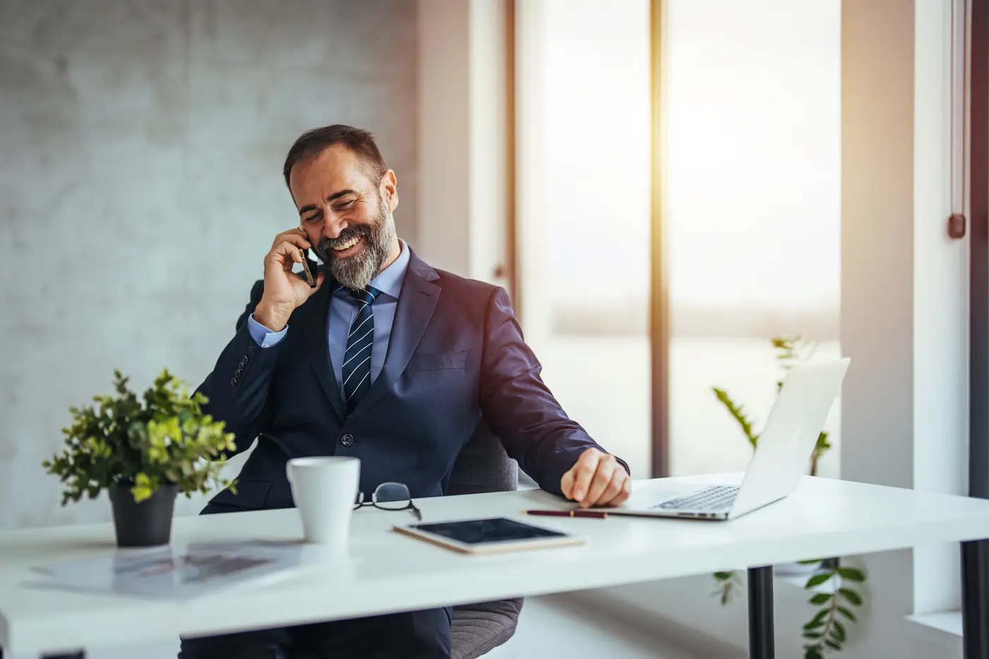 Professional financial advisor smiling while speaking with a client by phone at a modern desk, representing responsive guidance and personalized retirement planning support.