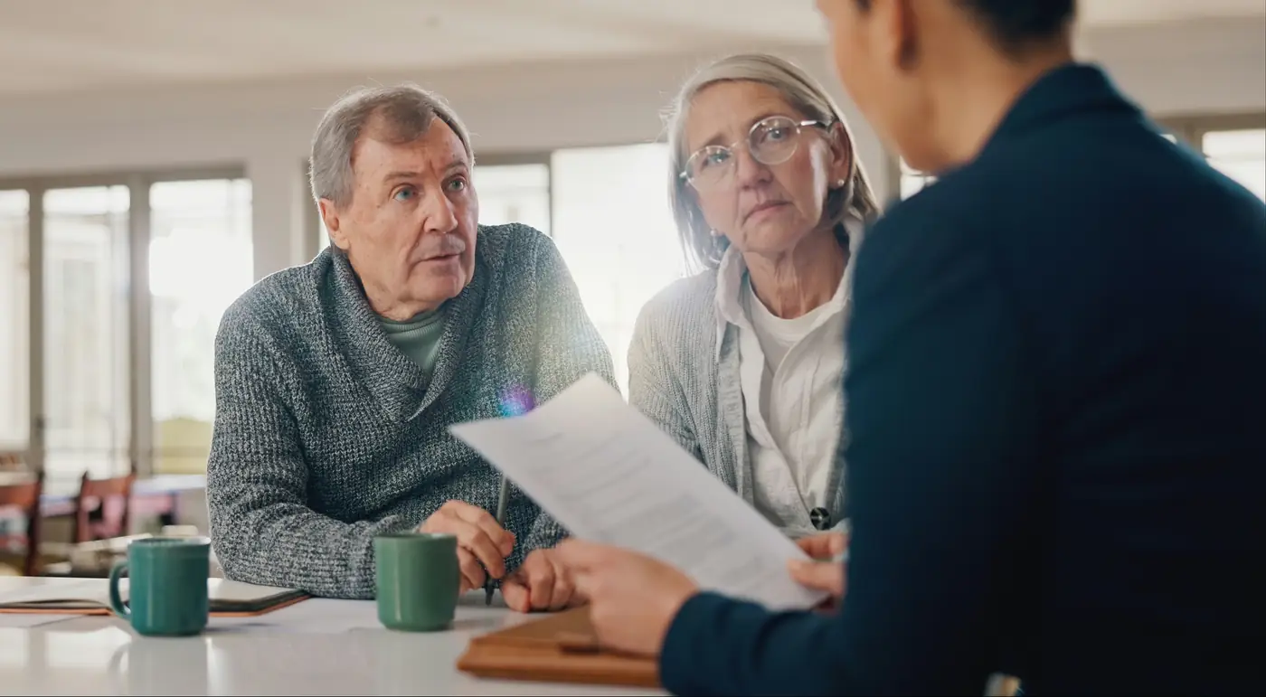 Retired couple meeting with a financial advisor to review documents and discuss retirement income decisions, reflecting guidance through complex planning and long-term wealth management.